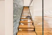 Freitragende Holztreppe mit Glasgeländer und markanter Natursteinwand